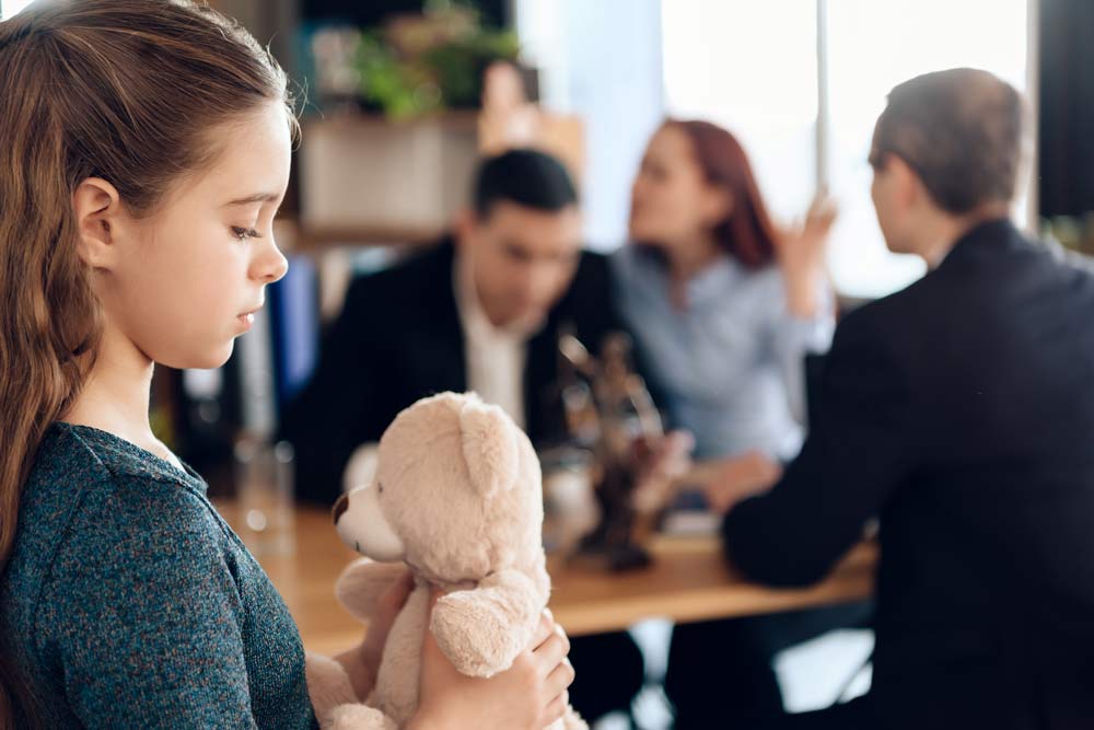 young girl, with group of adults arguing in the background